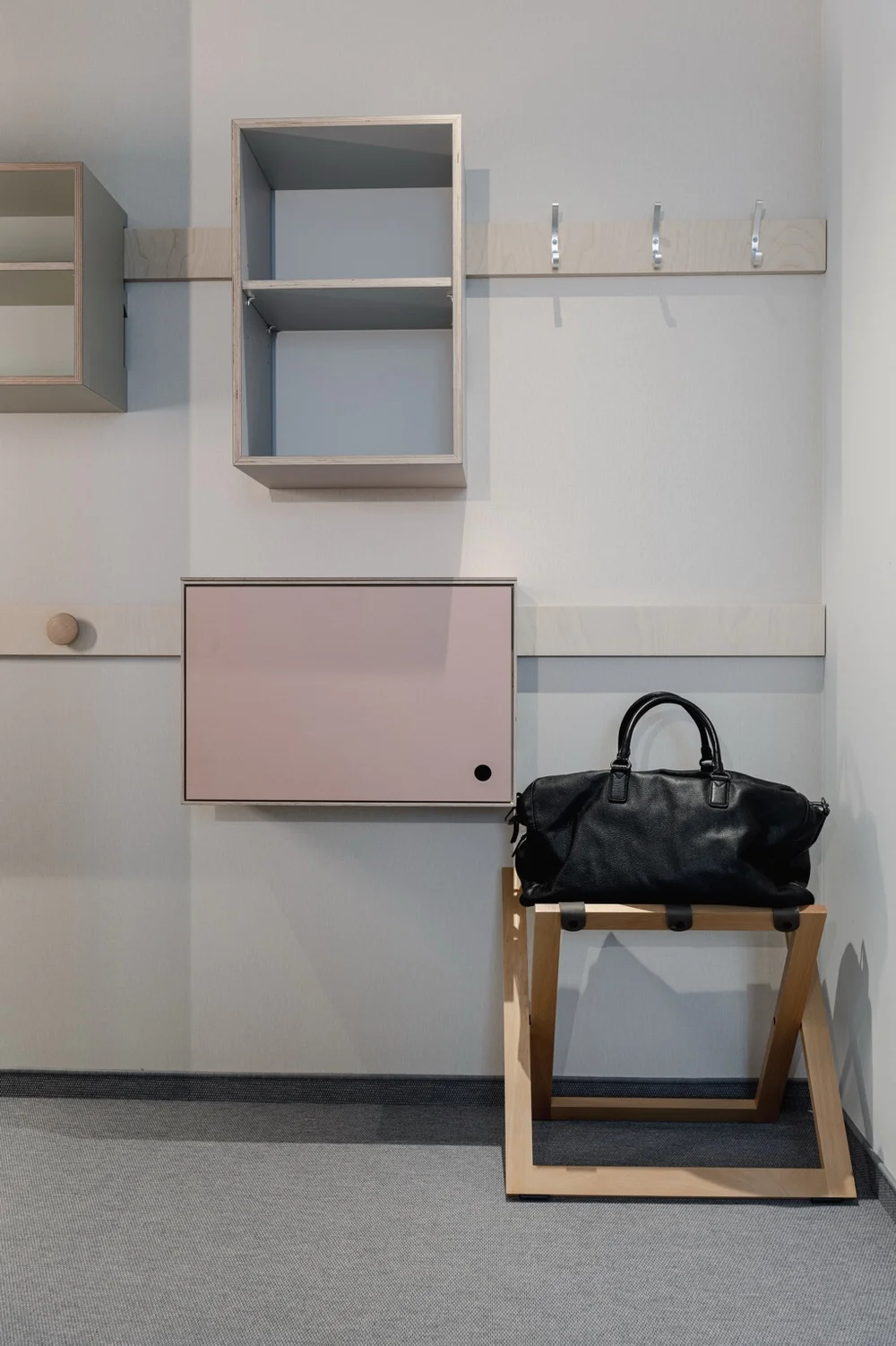 Offener Eingangsbereich im Hotel baltica Hamburg Altona mit Garderobe, offenen Regalen, Hakenleiste und schwarzer Reisetasche auf einem Holzgestell.