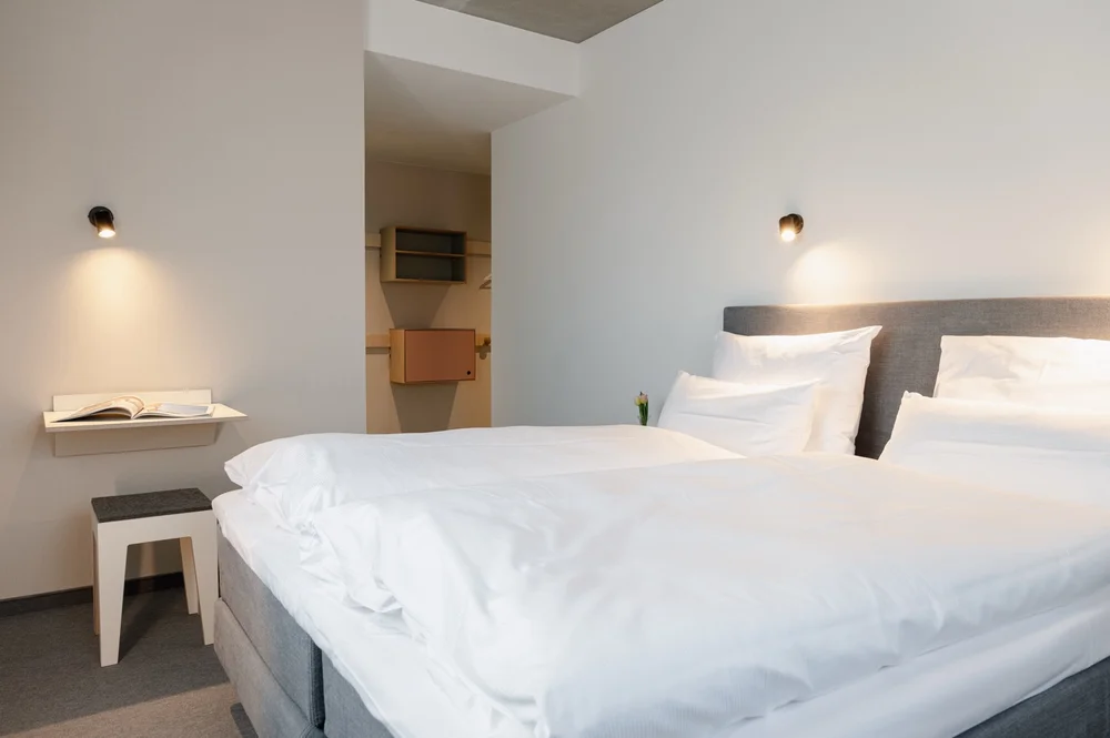 Gemütliches Hotelzimmer im Hotel baltica Hamburg Altona mit grauem Doppelbett, integrierter Leseecke, offenem Kleiderschrank und minimalistischem Design.