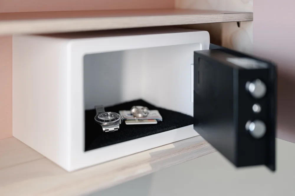 Offener Zimmertresor mit Uhr, Ringen und Karten im Inneren – sicher aufbewahrt in modernem Hotelzimmer.